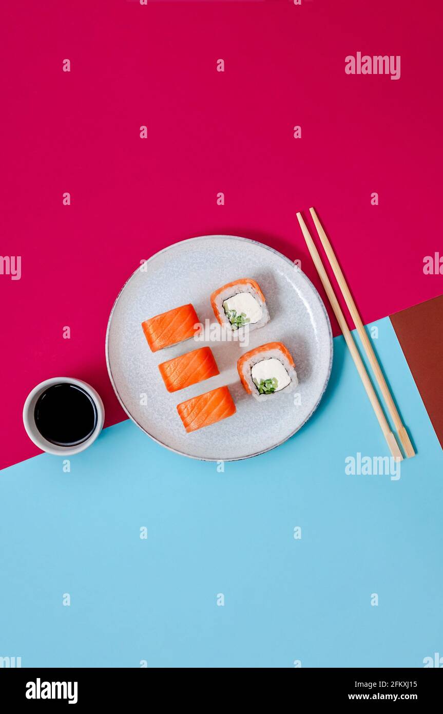 Panini Philadelphia con pesce salmone, cetriolo e formaggio sul piatto con salsa di soia su sfondo colorato. Concetto minimo Foto Stock