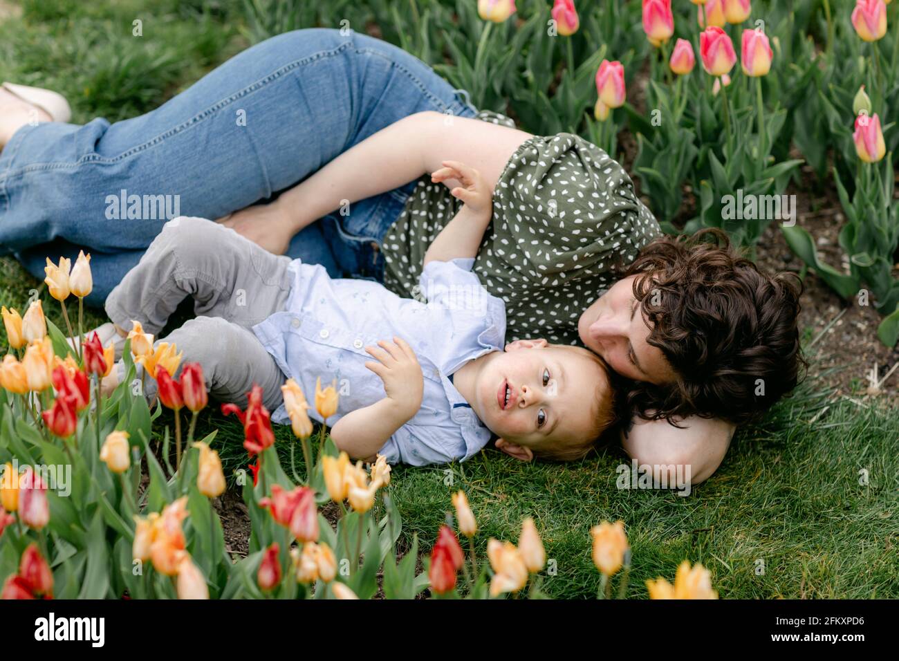Mamma che si stesa nell'erba con il figlio del bambino in tulipano giardino Foto Stock