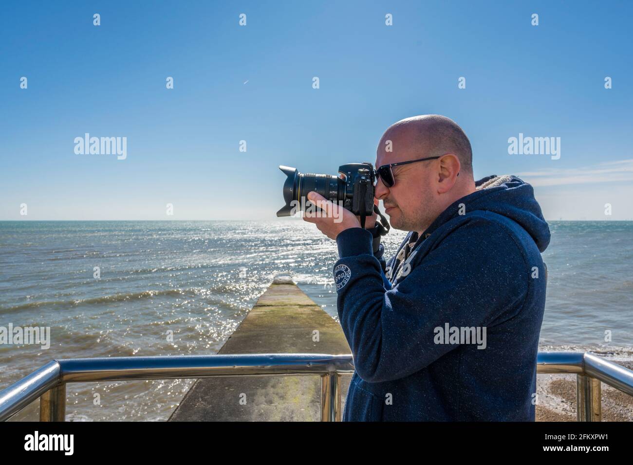 Il profilo sinistro del fotografo mentre scatta una foto con un mare sullo sfondo Foto Stock