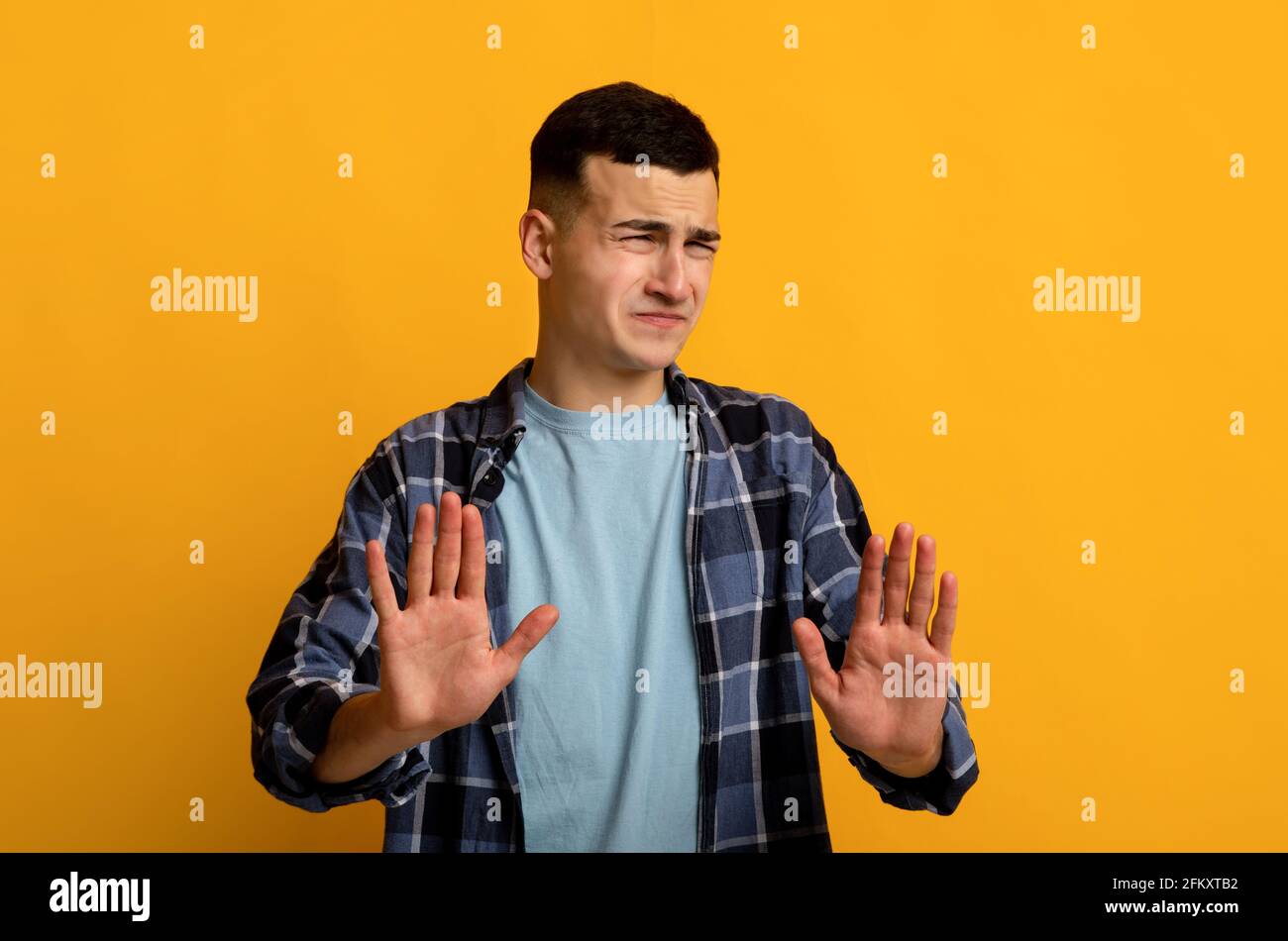 Ragazzo disgustoso millenario che mostra IL gesto DI STOP con entrambe le mani, esprimendo rifiuto su sfondo arancione studio Foto Stock