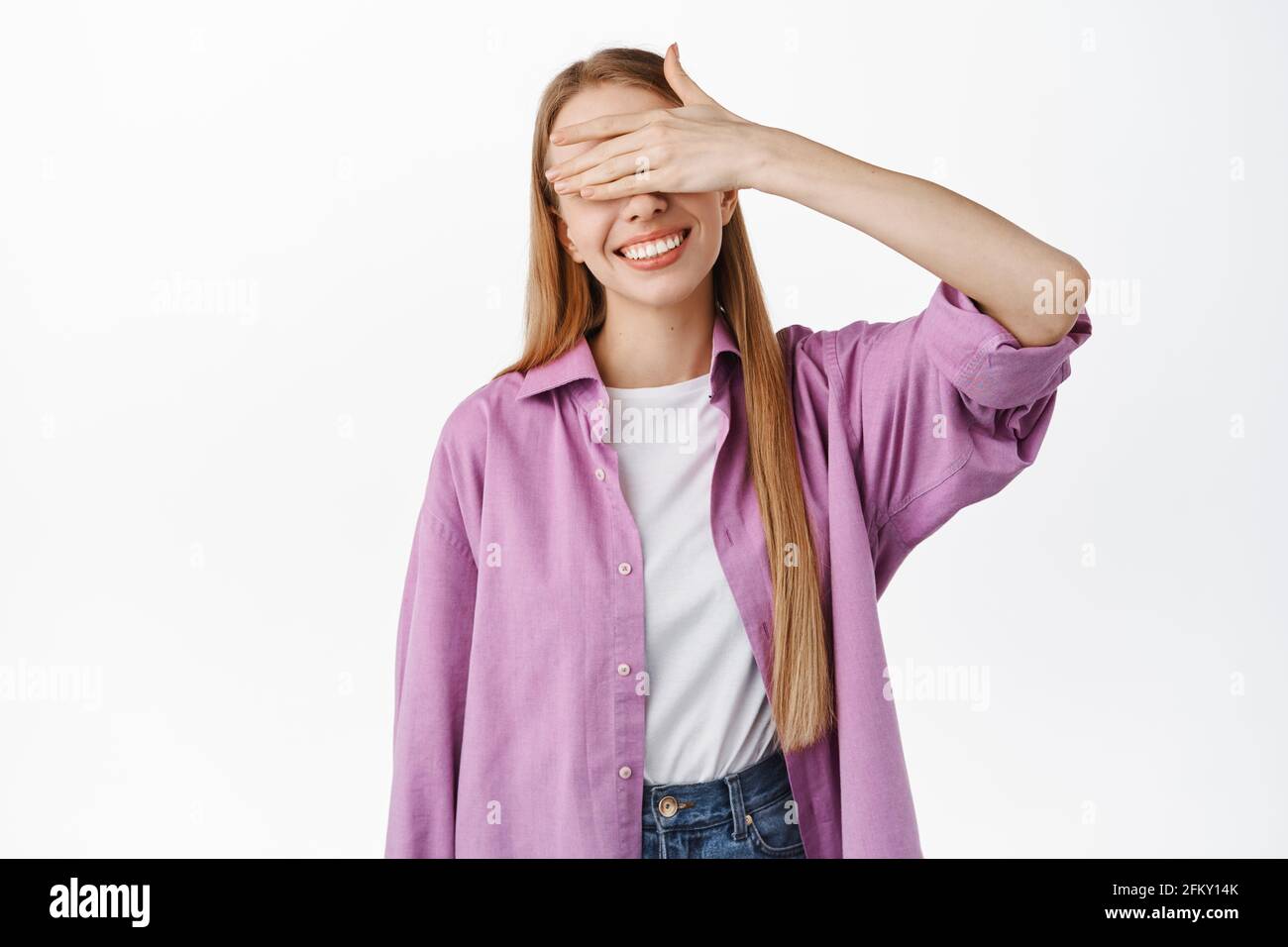 Immagine di bella giovane donna sognante, occhi di copertura e in attesa di sorpresa dono, anticipando, giocando nascondino n seek, in piedi su sfondo bianco Foto Stock