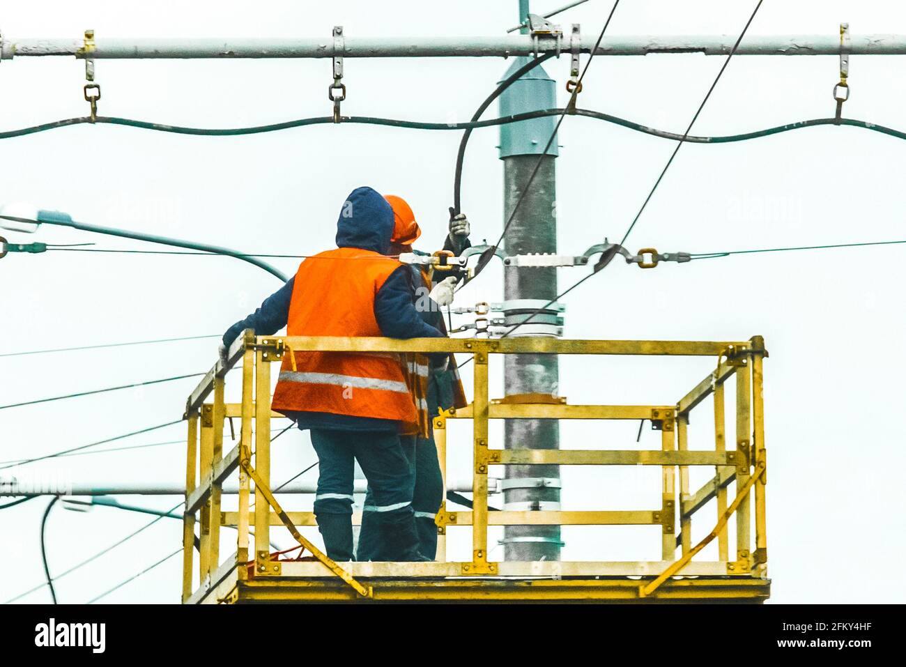 Due uomini di lavoro hanno sollevato la sicurezza su un'attrezzatura di gru di macchina che minaccia una linea elettrica di alimentazione. Foto Stock