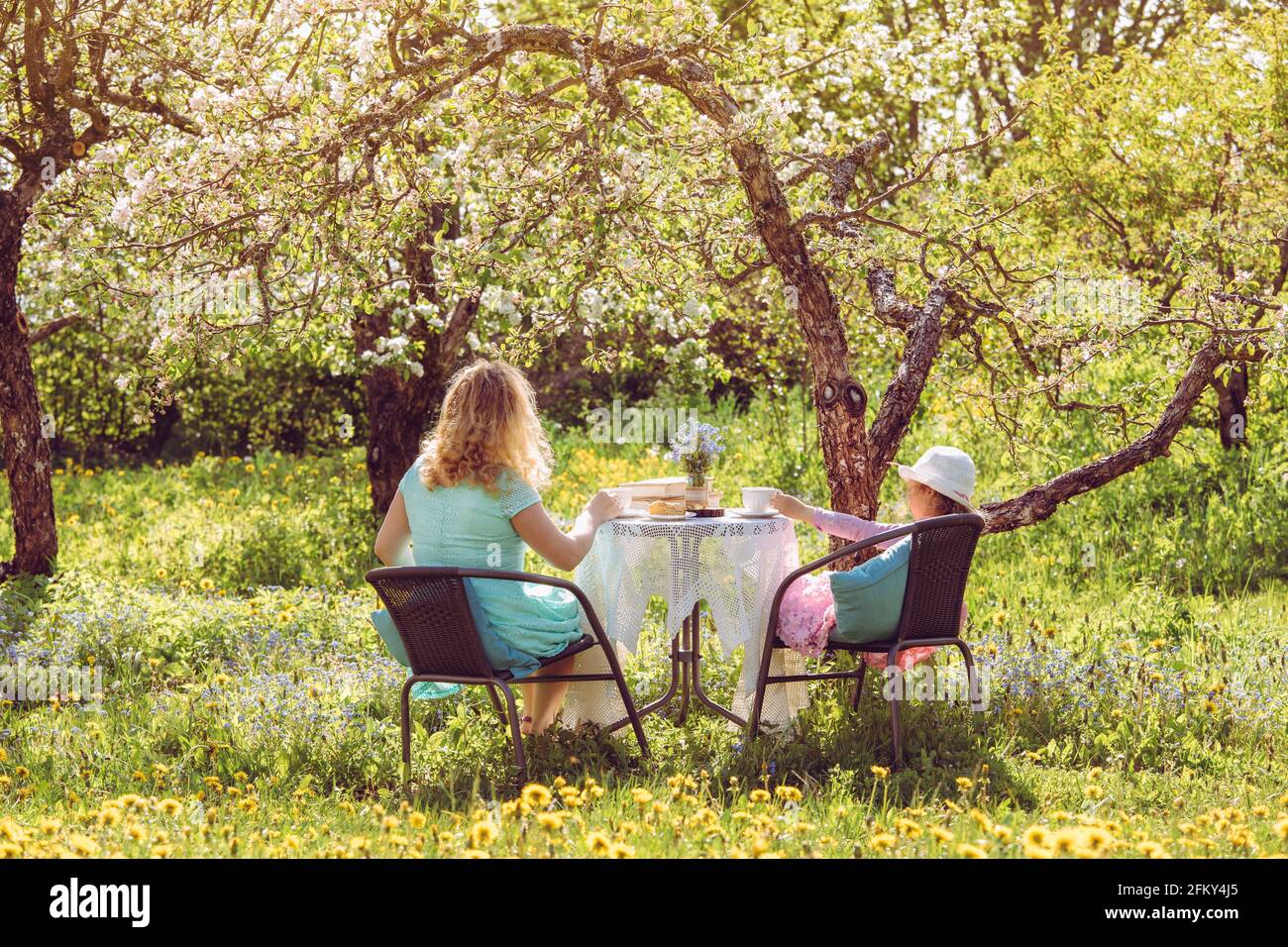 Madre figlia passare il tempo insieme in giardino sotto i fiori alberi di mela primavera, bere tè e trascorrere il tempo insieme. Idilliaco set di sole giorno Foto Stock