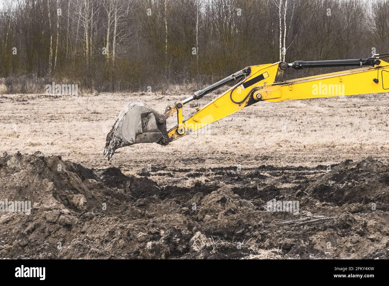 Benna dell'escavatore che scava una trincea nel terreno in un cantiere. Lavori industriali di scavo con terreno e terreno. Foto Stock