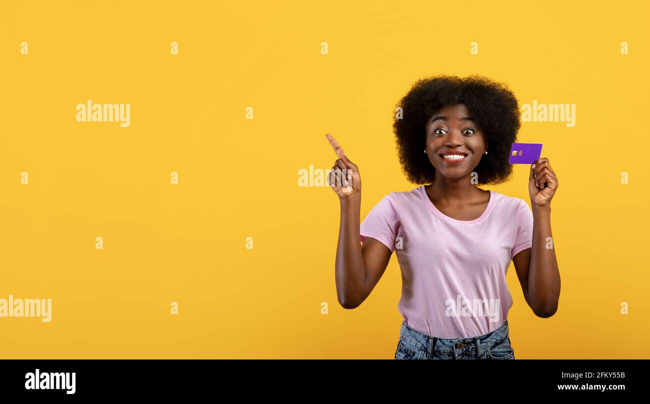 Concetto di pubblicità. Donna afroamericana che tiene la carta di credito e che punta allo spazio vuoto su sfondo giallo Foto Stock