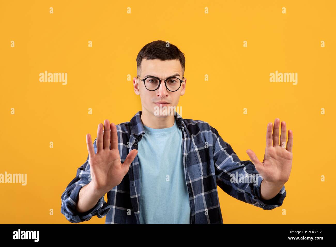 Mantenga la vostra distanza. Irritato giovane ragazzo in occhiali che mostrano il gesto DI STOP con entrambi i palmi a fotocamera su sfondo arancione Foto Stock
