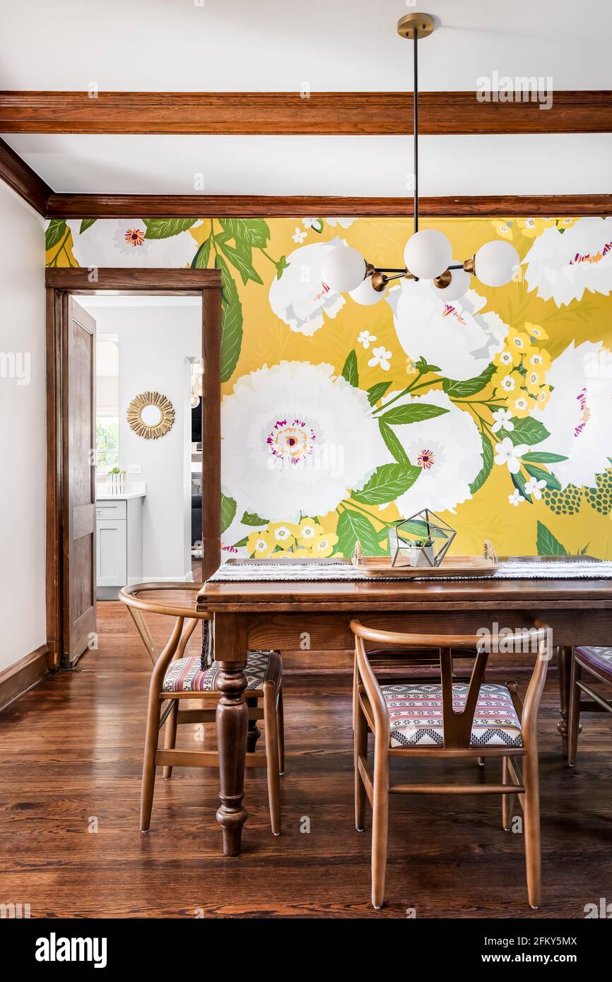 Una sala da pranzo con una moderna luce appesa al soffitto. Una vibrante  carta da parati floreale si trova sulla parete lontana con travi di legno  scuro sul soffitto Foto stock -
