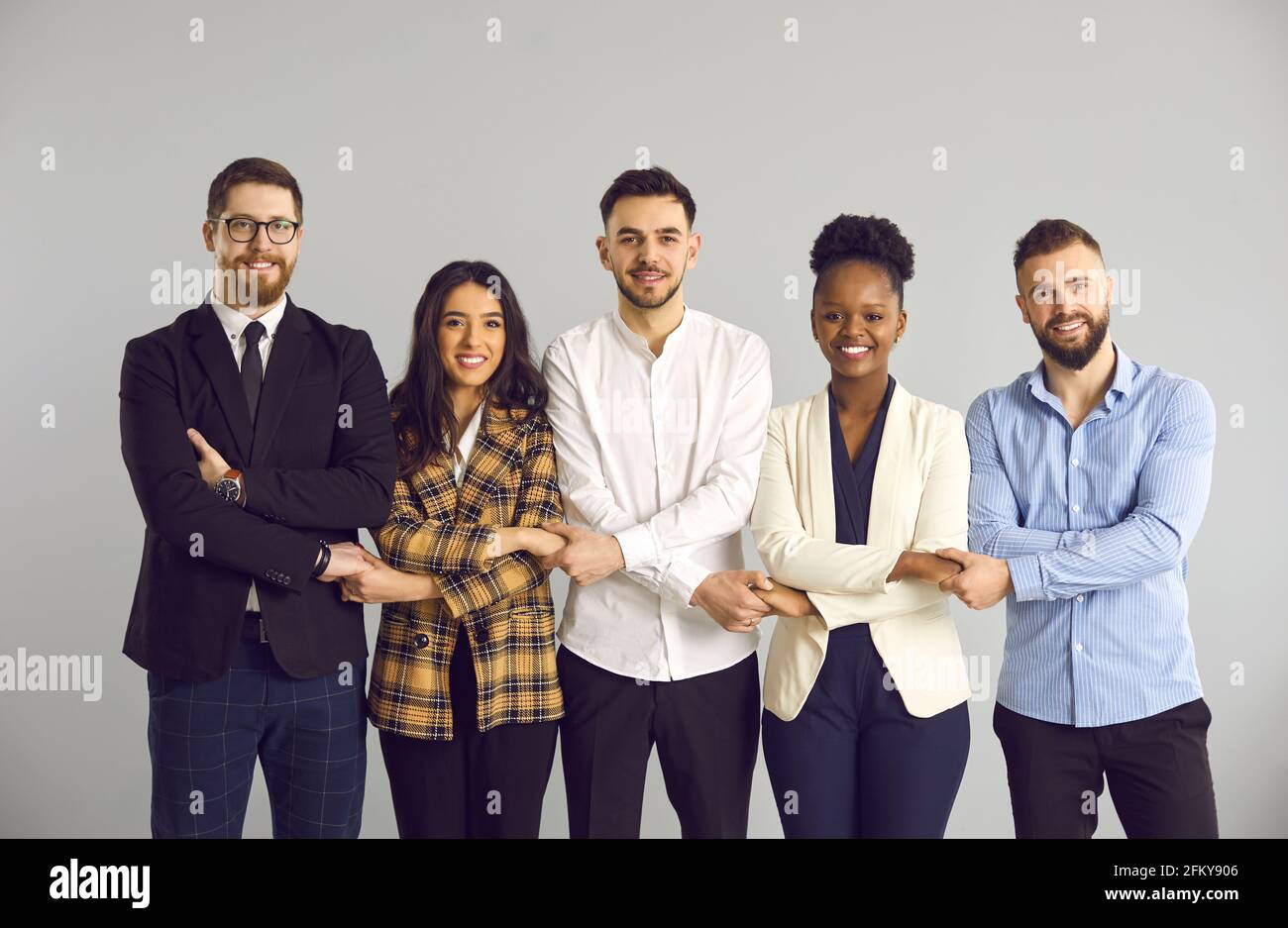 Gruppo di giovani uomini d'affari diversi sorridenti in fila e tenendo le mani Foto Stock