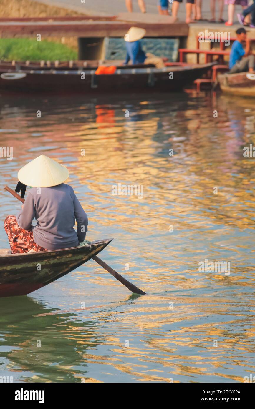 Una donna vietnamita locale che indossa un cappello a foglia conica tradizionale (non la) pagaie nel fiume Thu Bon nel pittoresco villaggio storico di Hoi An, Vietnam. Foto Stock