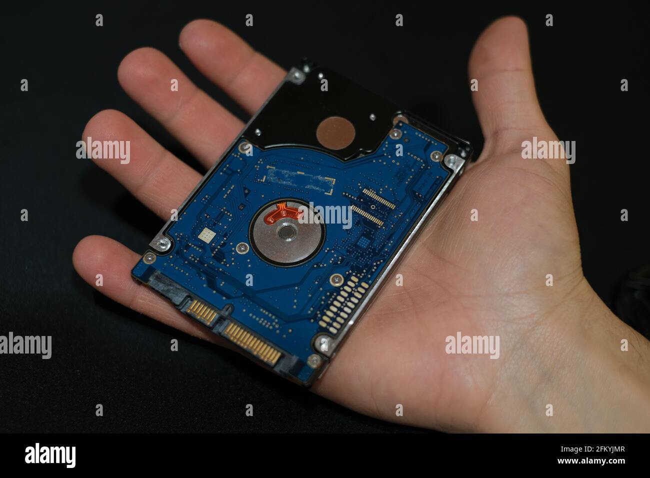 Mano dell'uomo tenere un dispositivo di memorizzazione hdd al buio superficie, componenti tecnici, parti per la sicurezza dei dati Foto Stock
