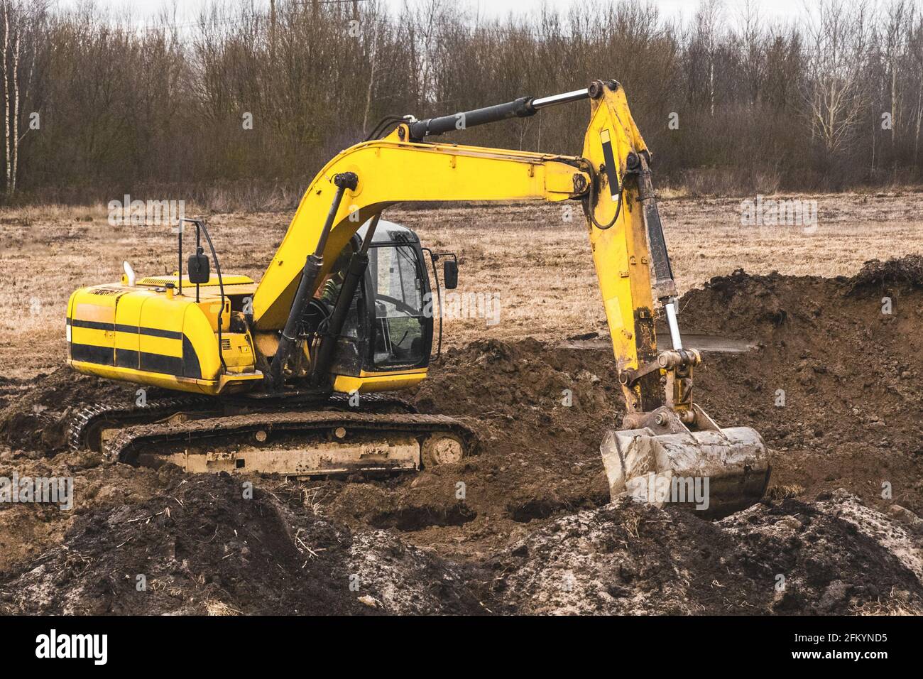 Il lavoratore di costruzione su un'attrezzatura di escavatore cingolato scava una trincea in un'area industriale. Lavori di scavo con terra e suolo. Foto Stock