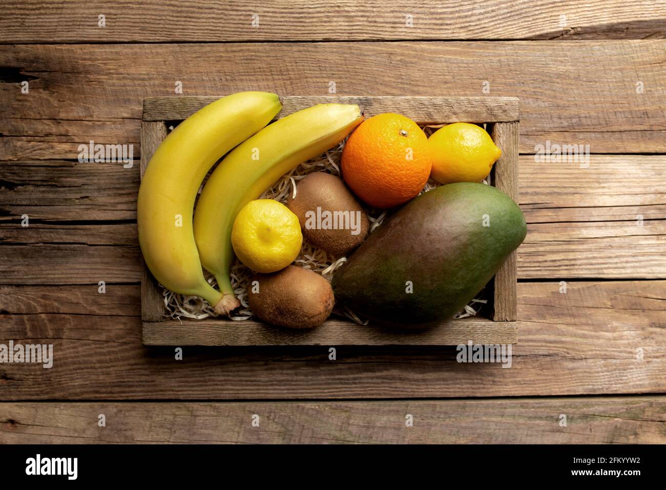 Frutta tropicale fresca in una scatola di consegna di legno su sfondo di legno. Arancione, banana, mango, kiwi e limone vista dall'alto piatto con spazio per la copia per som Foto Stock