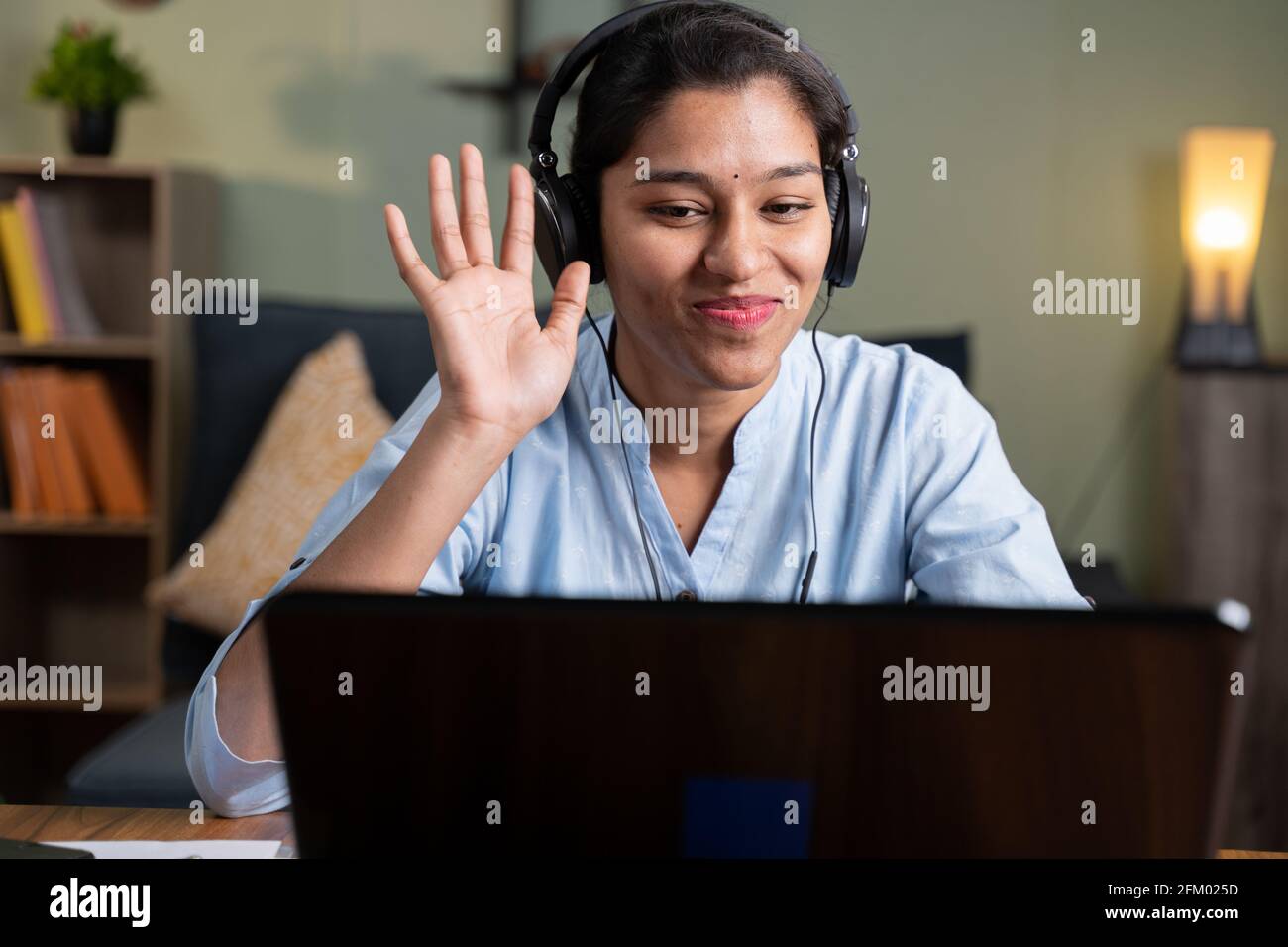 Giovane donna d'affari in riunione online salutando hai in videoconferenza mentre si lavora da casa - concetto di video chat, conferenza o vlogging Foto Stock