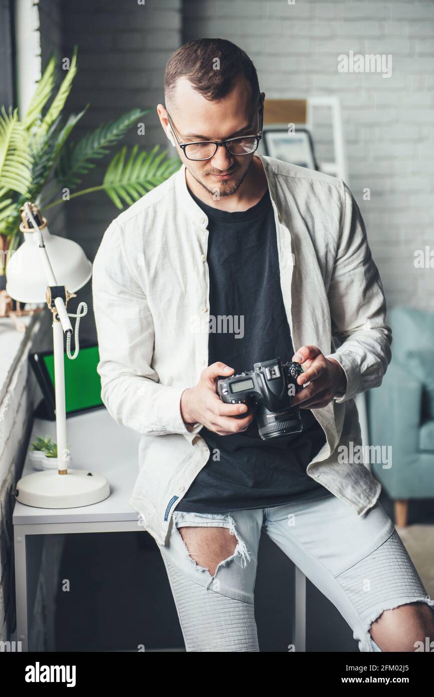 Il fotografo di balding sta usando una macchina fotografica a casa che indossa occhiali mentre si guarda lo schermo Foto Stock
