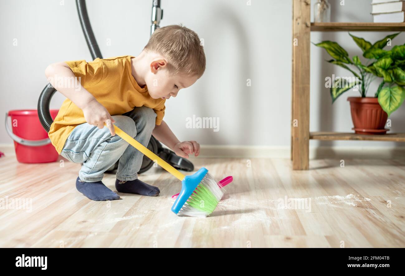 Un bambino carino aiuta nella pulizia della casa vicino spazzare la  spazzatura con una scopa per bambini dal pavimento in una casseruola  giocattolo Foto stock - Alamy