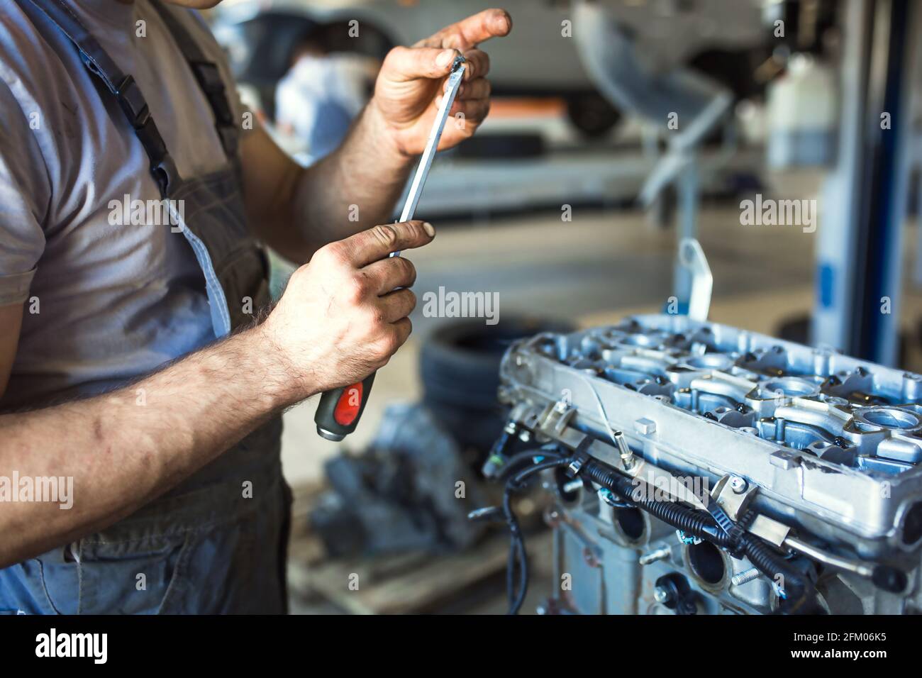La mano di un addetto alla riparazione dell'auto con le chiavi e un attrezzo speciale sullo sfondo dell'area di manutenzione. Un meccanico ripara il motore in una stazione di servizio auto Foto Stock