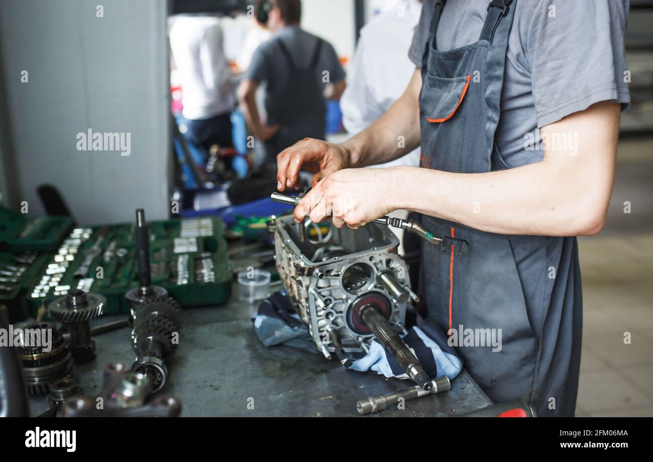 La mano di un addetto alla riparazione dell'auto con le chiavi e un attrezzo speciale sullo sfondo dell'area di manutenzione. Un meccanico ripara il motore in una stazione di servizio auto Foto Stock
