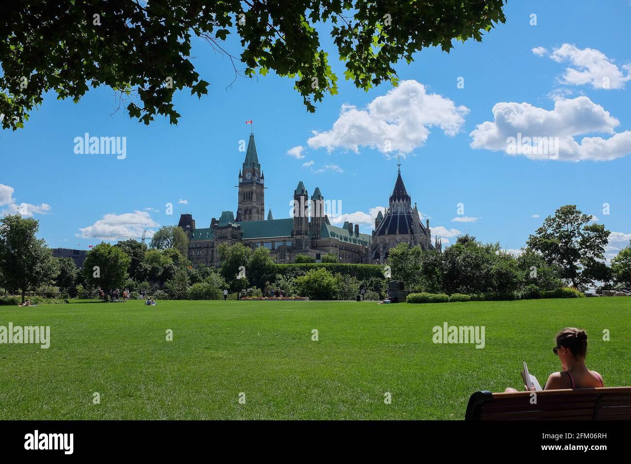 Donna seduta in un parco di fronte a Parliament Hill, visto da Confederation Park, a Ottawa, Ontario, Canada Foto Stock