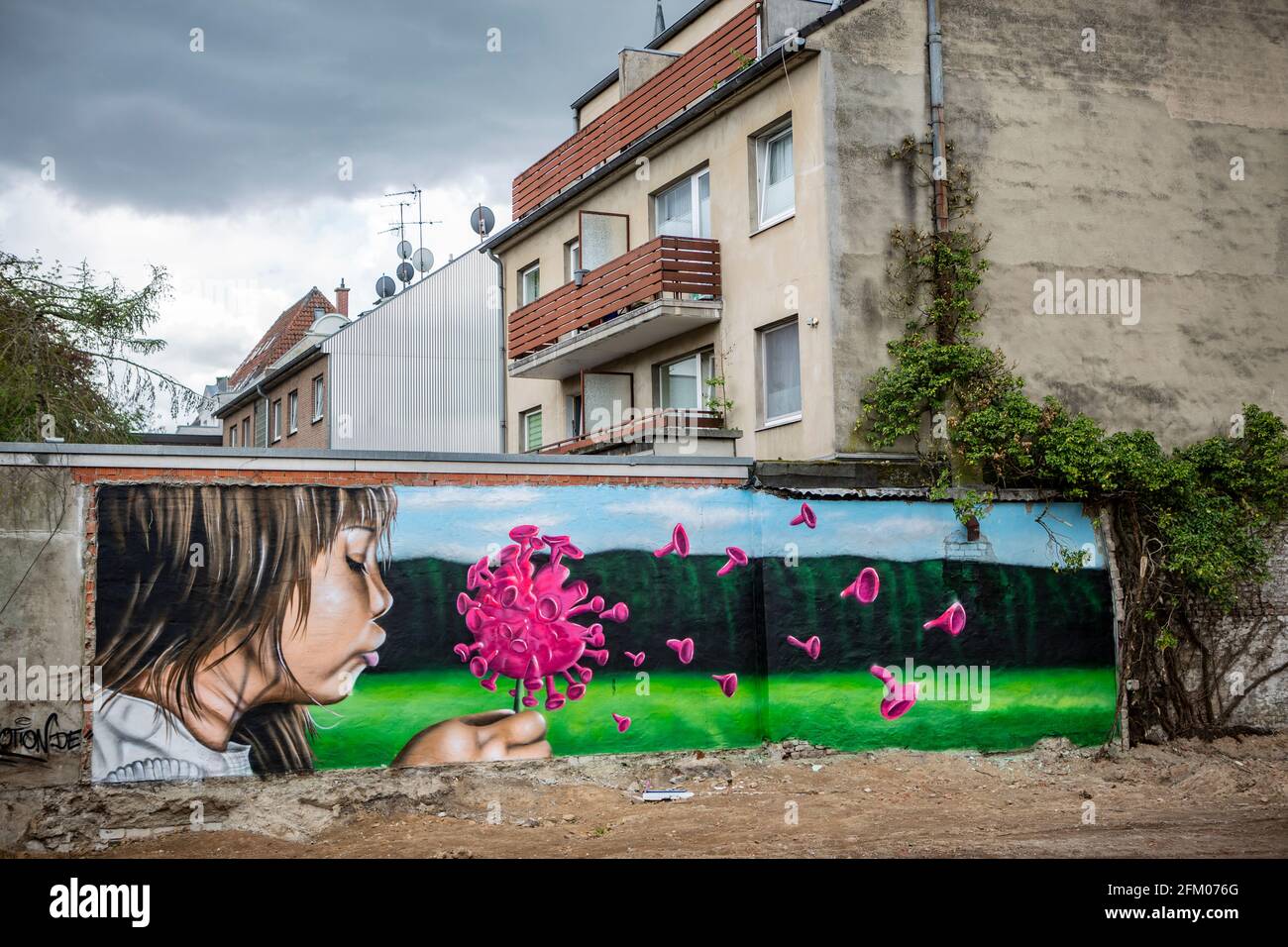 Ein Graffiti an einer alten Mauer zeigt ein Mädchen, welches wie bei einer Pusteblume ein Coronavirus anpustet, welches dann auseinander fliegt. Ein s Foto Stock