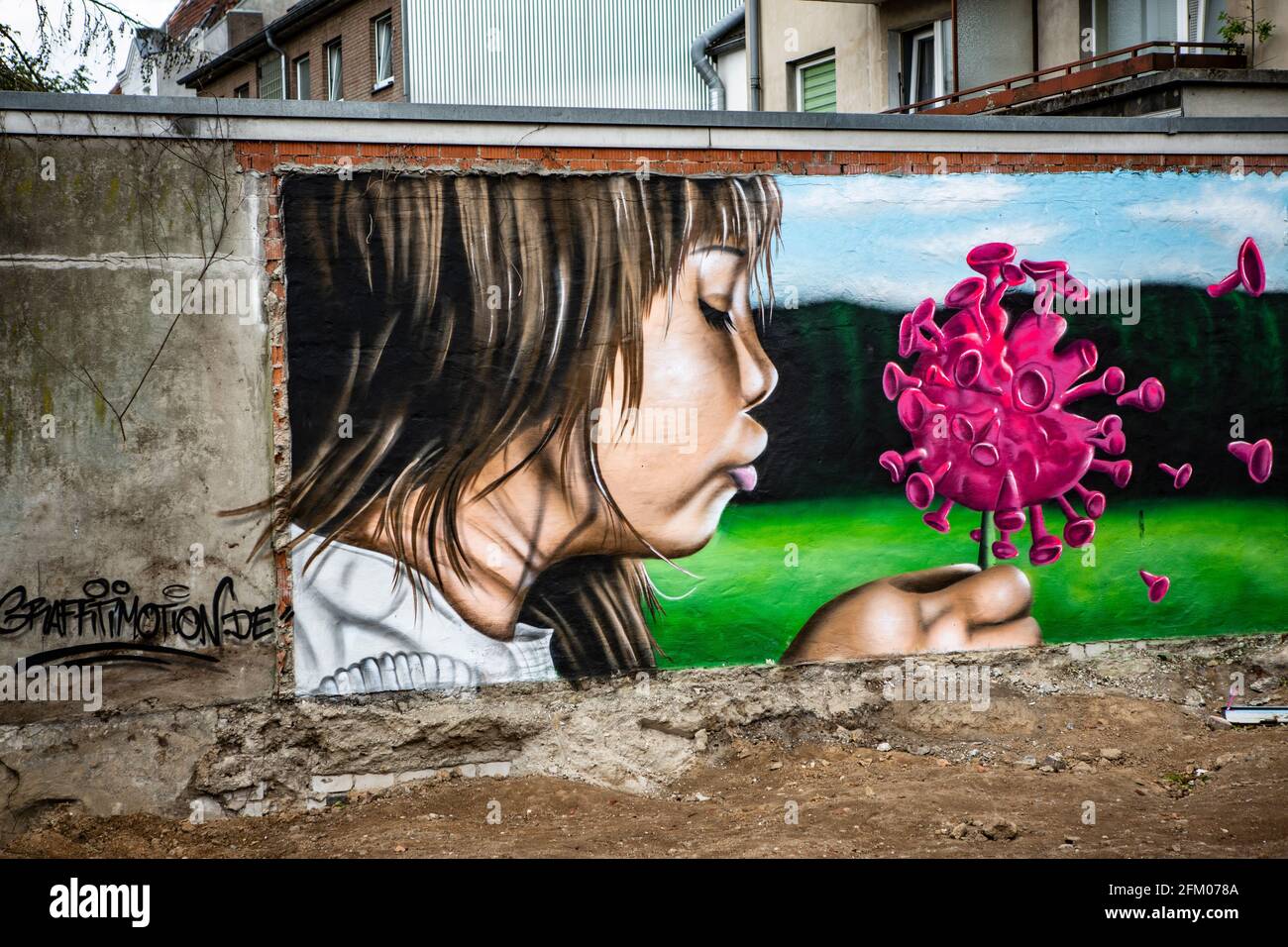 Ein Graffiti an einer alten Mauer zeigt ein Mädchen, welches wie bei einer Pusteblume ein Coronavirus anpustet, welches dann auseinander fliegt. Ein s Foto Stock