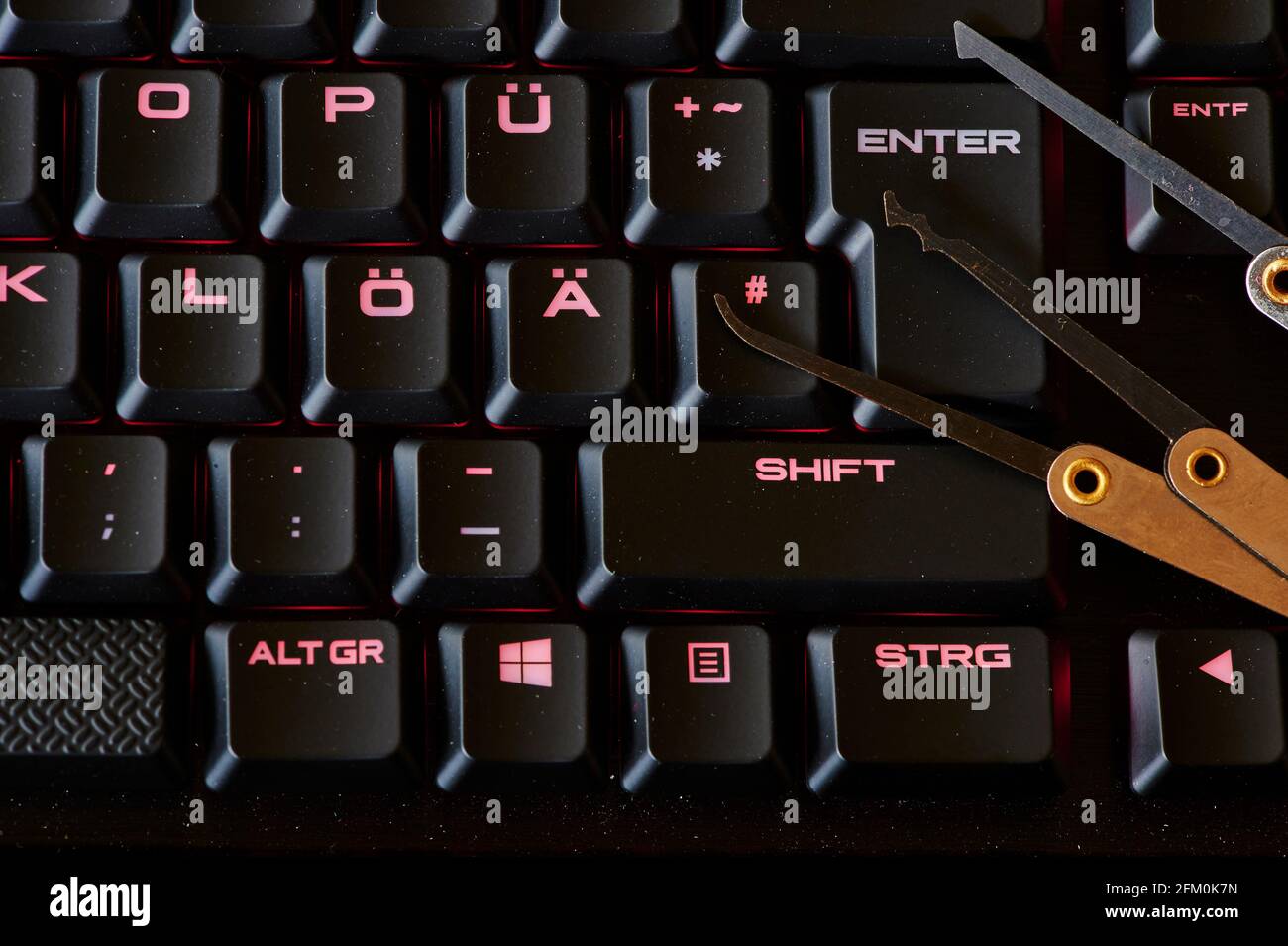 Berlino, Germania - 24 aprile 2021: Ambiente oscuro con una tastiera illuminata e vari strumenti di rodaggio che simboleggiano la criminalità informatica. Foto Stock