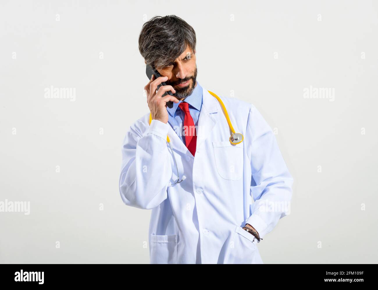 Ritratto a metà corpo di un bel medico utilizzando il cellulare su sfondo bianco. Foto Stock