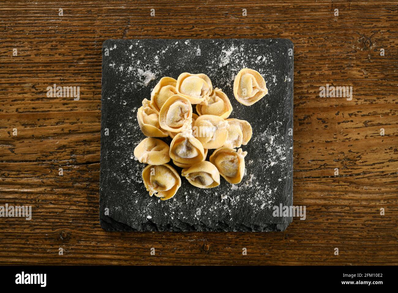 Vista dall'alto della tradizionale pasta italiana di cappelletti fatti a mano su nero tavola cosparsa di farina posta su tavola di legno Foto Stock