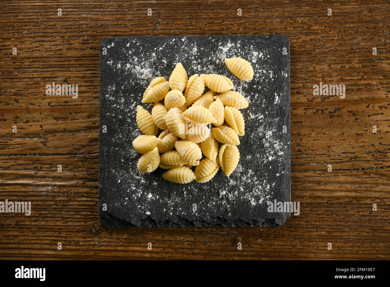 Vista dall'alto di mucchio di gnocchetti sardi crudo con farina messa a bordo su tavolo di legno Foto Stock