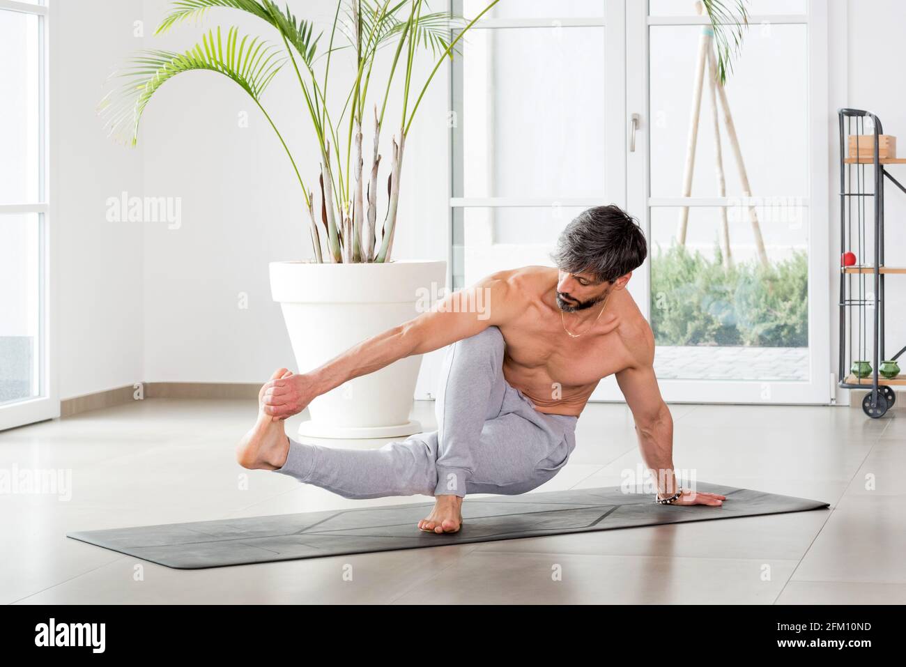 L'uomo sportivo atletico che fa un equilibrio di yoga posa stretching a. afferra le dita dei piedi per aumentare la mobilità e rafforzare i muscoli in una palestra di alta chiave con copia Foto Stock