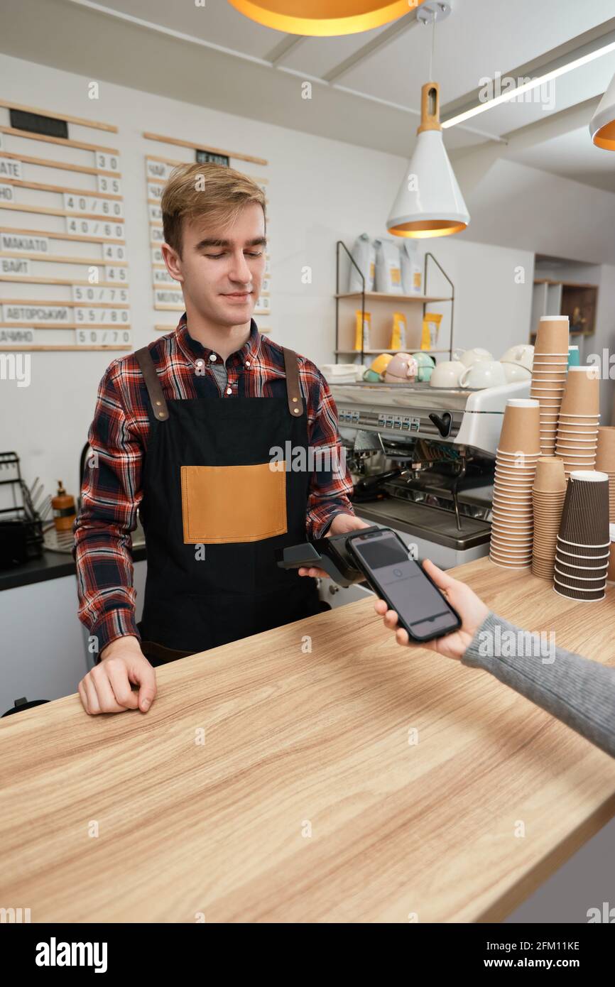 il cliente che tiene il telefono vicino al terminale nfc effettua il pagamento senza contatto. Foto Stock