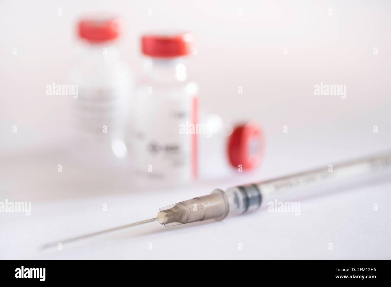 La siringa sottile si trova per flaconcini di vaccinazione singoli con tappo rosso su fondo bianco. Corona - Covid-19. Mettere a fuoco il mozzo grigio dell'ago Foto Stock