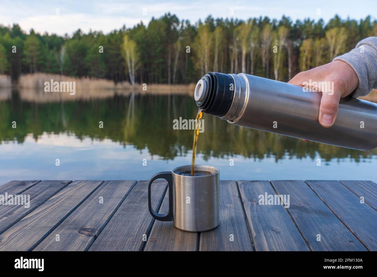 Versare il tè caldo in una tazza da un thermos la mattina accanto al lago e  alla foresta in primavera, primo piano. Natura e concetto di viaggio Foto  stock - Alamy