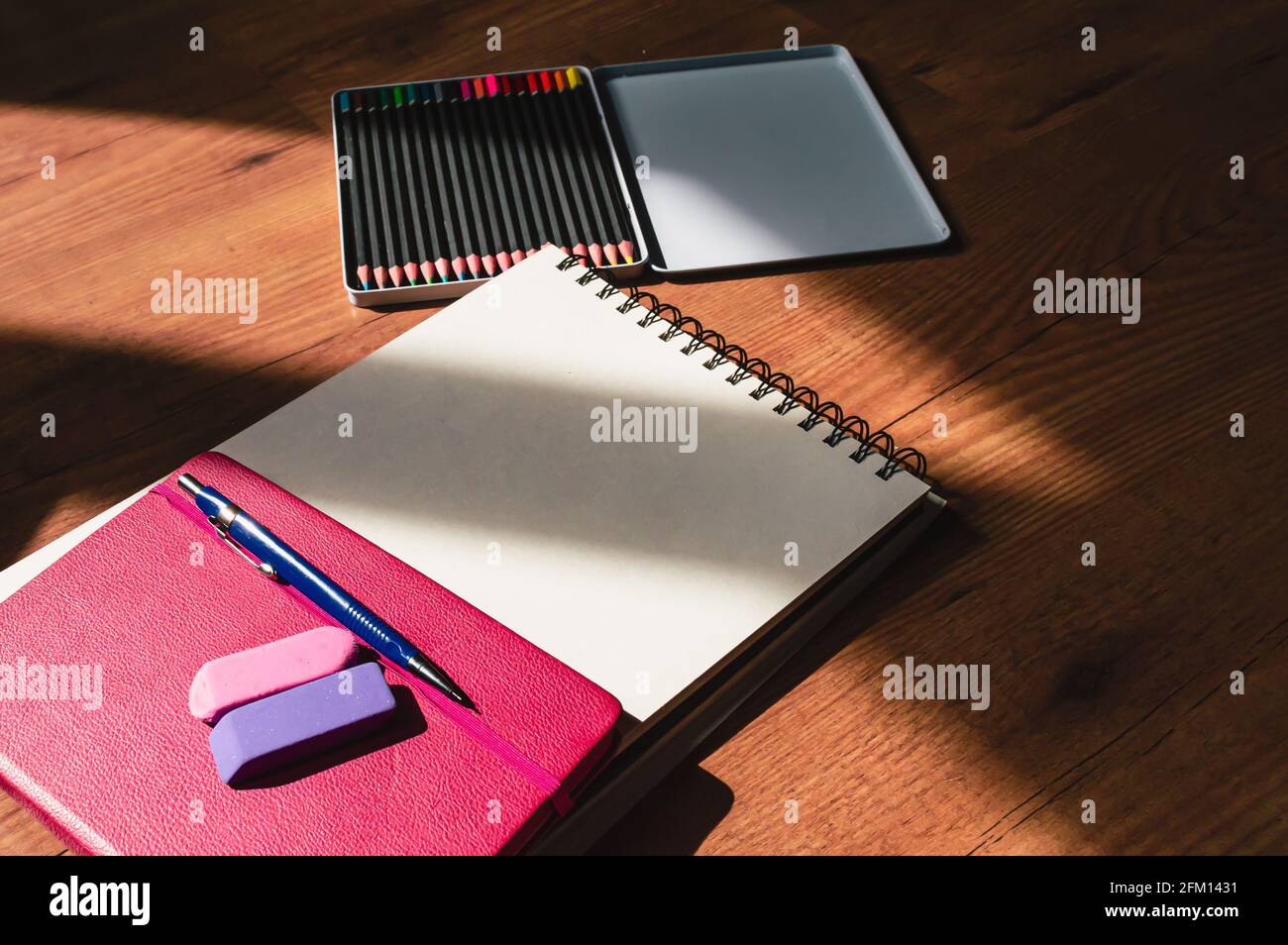 Immagine di un quaderno rosa, due cancellatori, una matita di riempimento, un quaderno e matite colorate incorniciate da ombre Foto Stock