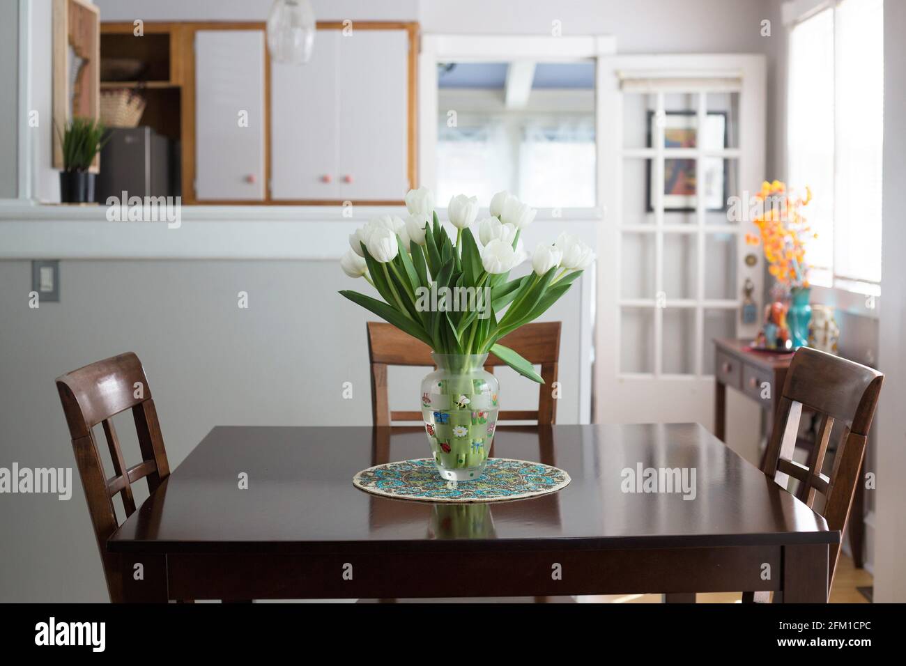 Un tavolo da pranzo con un vaso di vetro pieno di tulipani bianchi. Foto Stock