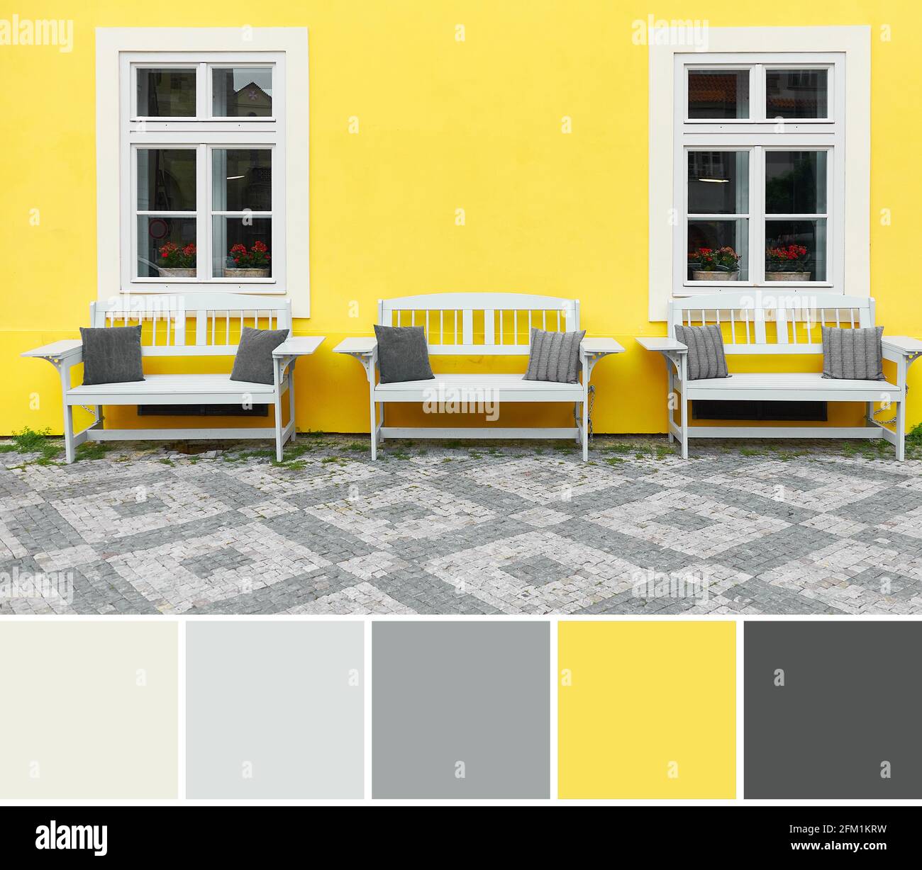 Tavolozza dei colori dell'immagine di viaggio di Praga. Illuminante casa dipinta di giallo con facciata classica e tre panchine di legno bianco. Colore di Foto Stock
