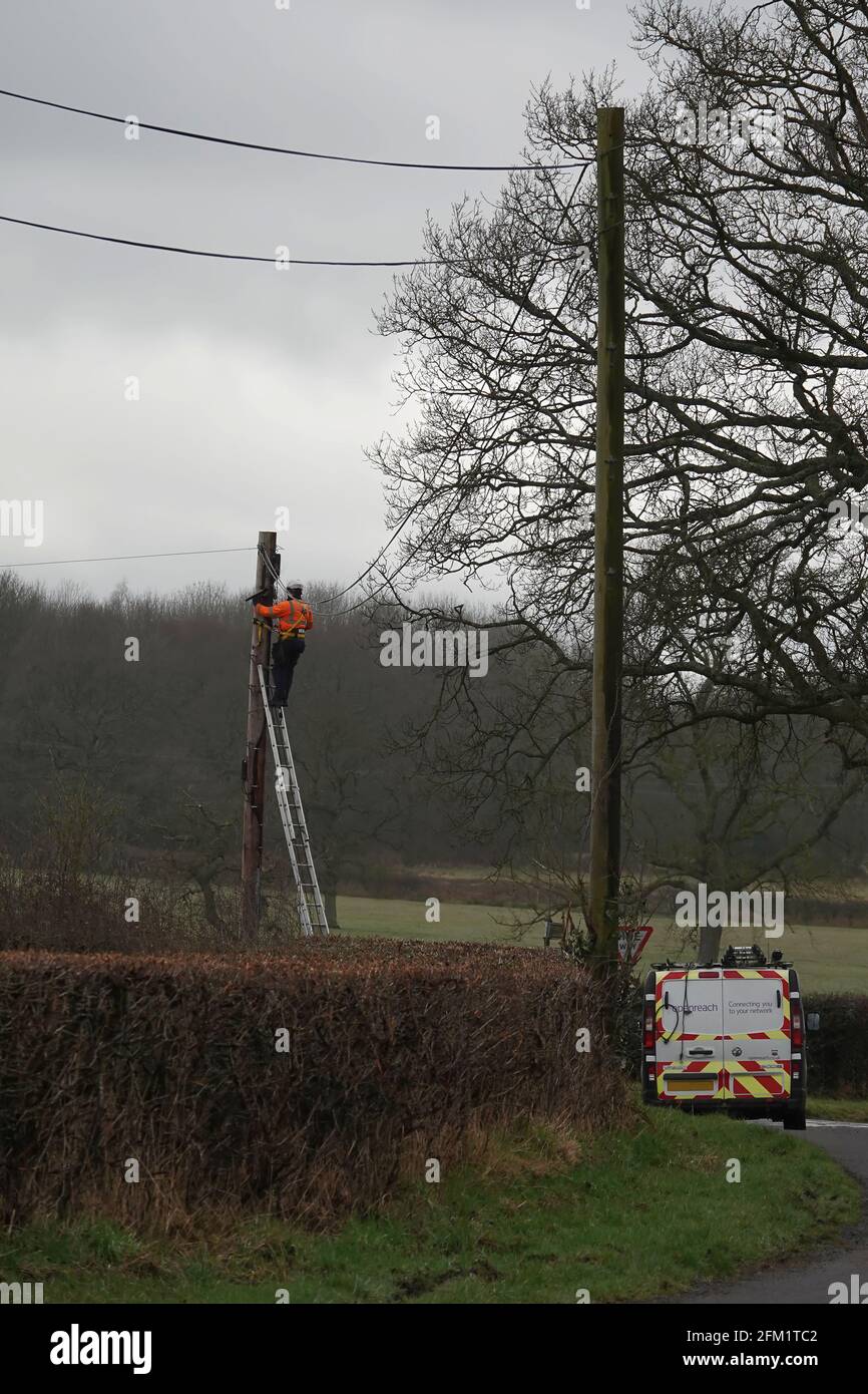 British Telecom Openreach ingegnere che lavora in altezza al top di un palo telegrafico in campagna Foto Stock