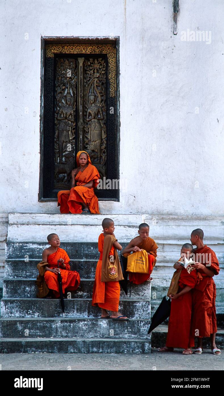 I novizi di un monastero buddista di Luang Prabang aspettano la prossima lezione di fronte ad una porta in legno decorata con sculture. 12/1996 - Christoph Kel Foto Stock