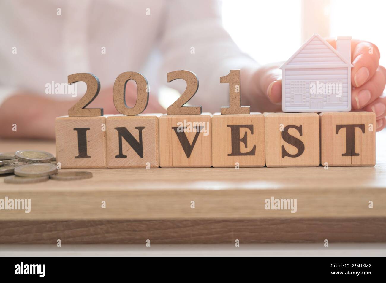 Investire in 2021 Concept. Investimento immobiliare e mutuo casa concetto finanziario, Word INVESTE e 2021 su cubetti di legno e casa in miniatura su legno ta Foto Stock