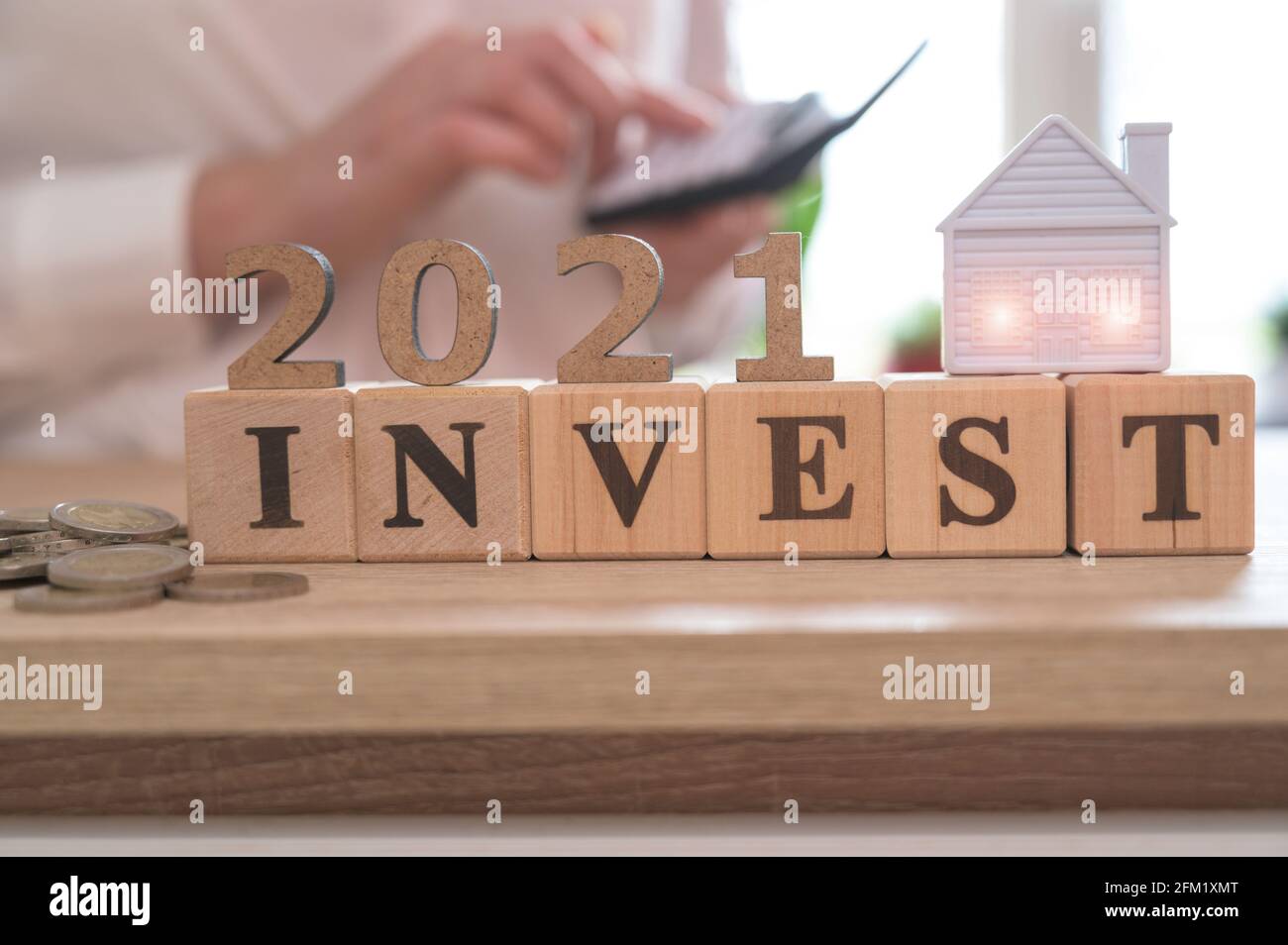 Investire in 2021 Concept. Investimento immobiliare e mutuo casa concetto finanziario, Word INVESTE e 2021 su cubetti di legno e casa in miniatura su legno ta Foto Stock