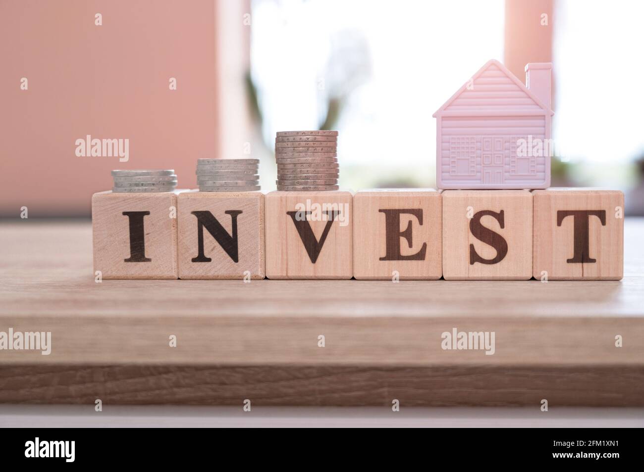 Investimento immobiliare e mutuo casa concetto finanziario, Word INVESTIRE su cubetti di legno e casa in miniatura su tavolo di legno. Concetto di investimento. Foto Stock