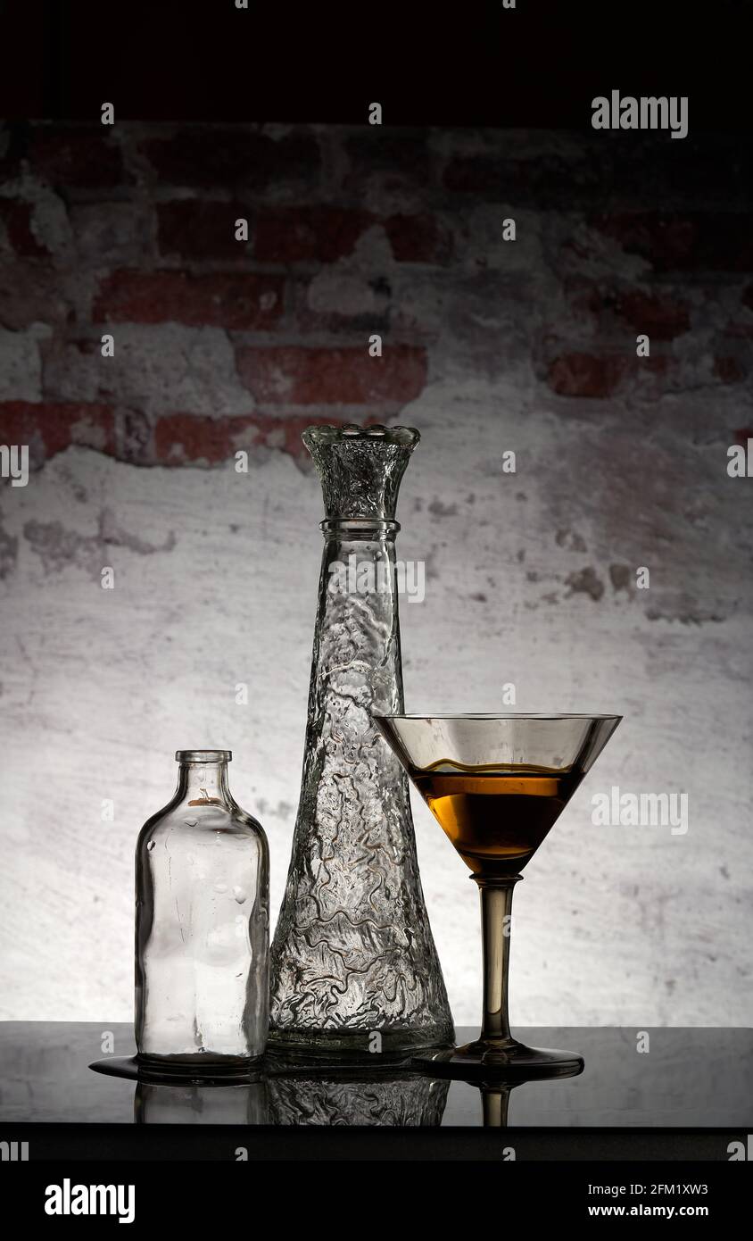 Vaso di vetro, vaso e vetro con la bevanda gialla su di esso davanti al fondo di mattoni. Immagine di Still Life. Foto Stock