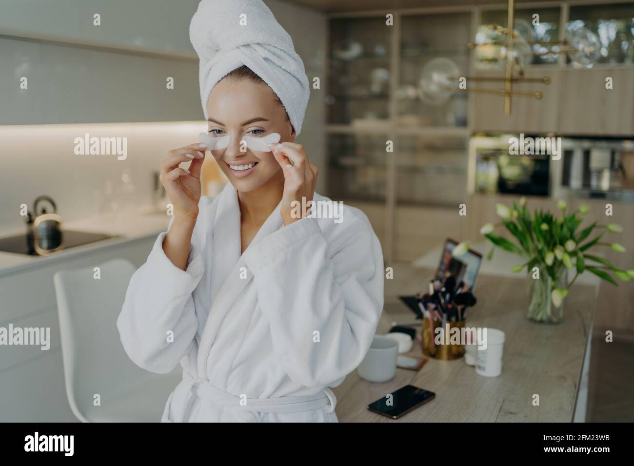 Donna felice in accappatoio e asciugamano sulla testa facendo la bellezza o procedure cosmetiche a casa Foto Stock