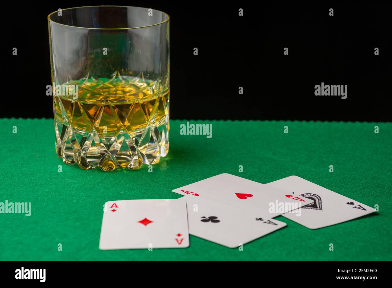 Primo piano di vetro con whiskey su tappetino verde con aces sfocati, sfondo nero, orizzontale, con spazio di copia Foto Stock