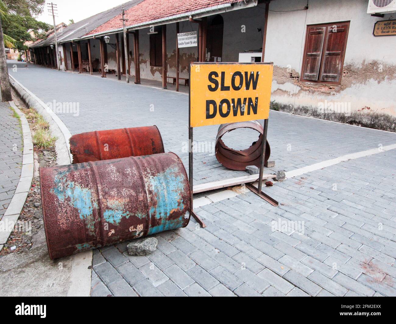 Sulle strade del vecchio quartiere storico, un cartello giallo dipinto in metallo lento verso il basso con barili arrugginiti. A Galle, Sri Lanka Foto Stock