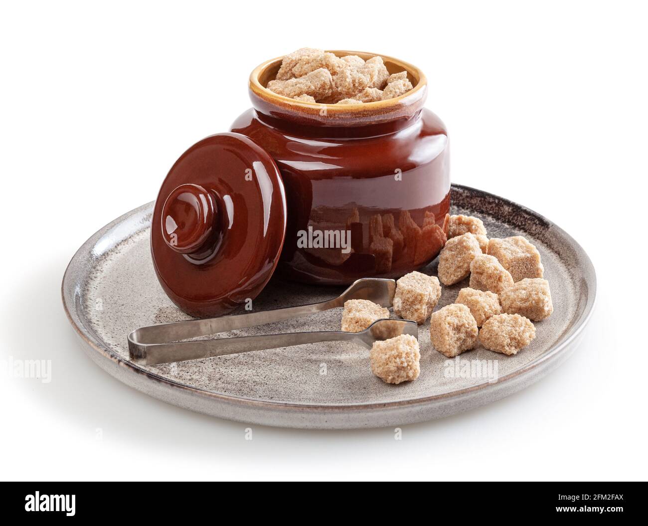 Cubetti di zucchero di canna di covata nel recipiente dello zucchero su ceramica piastra isolata su sfondo bianco Foto Stock