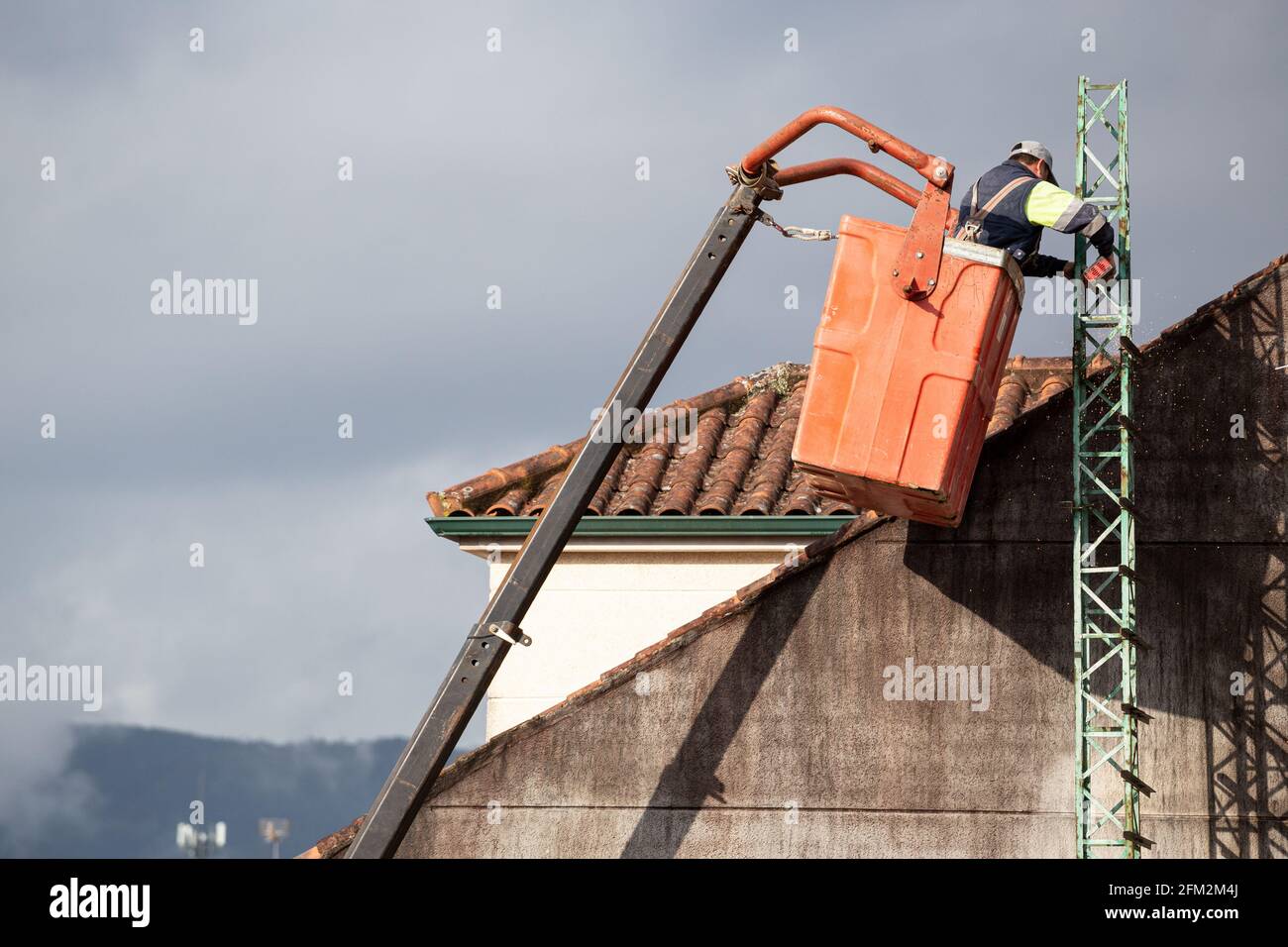 Lavorare su un elevatore telescopico che lavora con una smerigliatrice angolare un tetto di un edificio Foto Stock