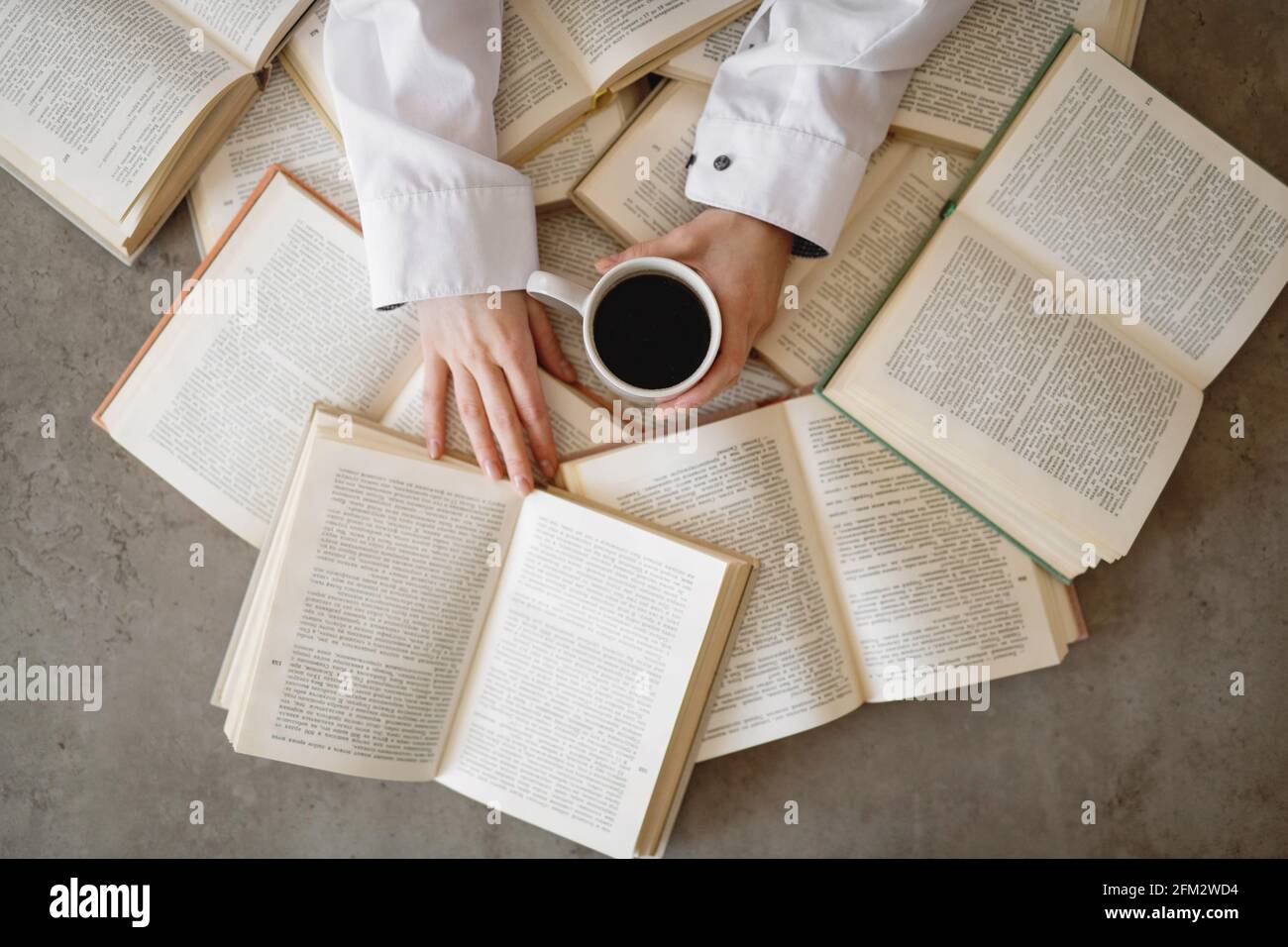 Le mani femminili tengono una tazza di caffè con un libro sullo sfondo. Foto Stock