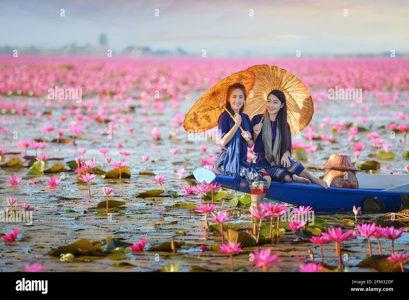 Due belle donne che navigano su un lago con fiori di loto rosa, Thailandia Foto Stock