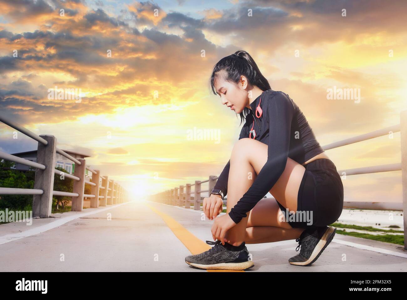 Donna runner accovacciata su un ponte che guarda il suo orologio intelligente all'alba, in Thailandia Foto Stock