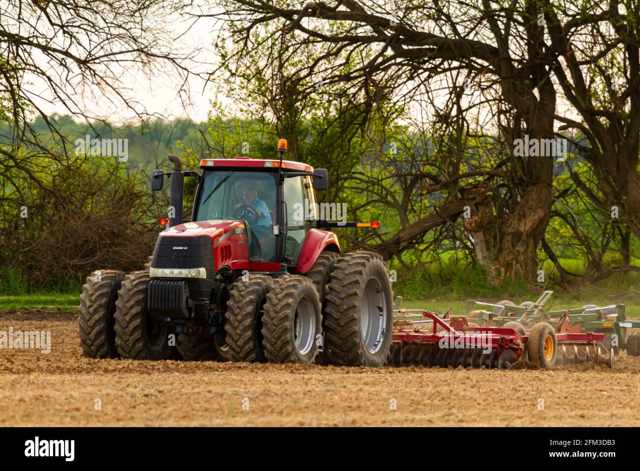 Chestertown, MD, USA 05-02-2021: Il trattore Case IH Magnum 305 a sei ruote rosse con cabina sta arando un campo agricolo vuoto in primavera. L'aratro a. Foto Stock